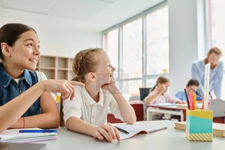 Two girls, surrounded by books and colorful school supplies, actively engage in a classroom discussion
