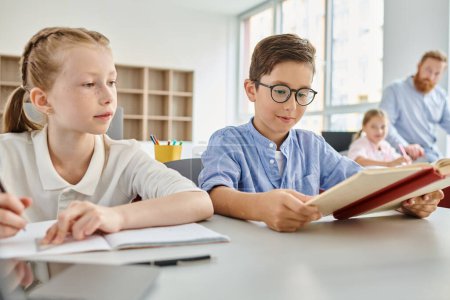 Un niño y una niña sentados en una mesa, absortos en la lectura de un libro juntos en un ambiente de aula brillante.