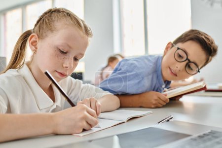Ein junges Mädchen und ein Junge voller Gedanken, während sie in einem lebhaften Klassenzimmer ihre Hausaufgaben erledigen.