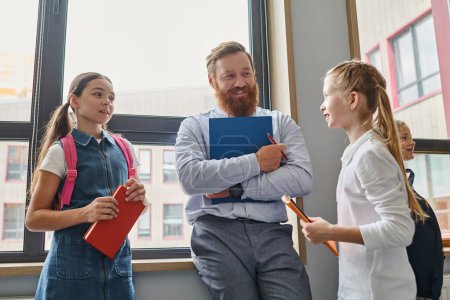 Photo for A man teacher instructs a kids in a bright, lively classroom setting as they stand next to each other with unity. - Royalty Free Image