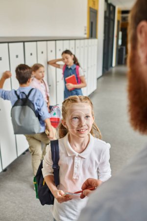 children eagerly check lockers in a lively hallway, guided by a male teacher in a bright classroom setting.