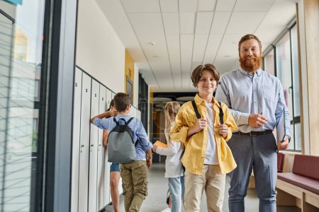 Un homme enseignant énergise un groupe d'enfants alors qu'ils marchent dans un couloir lumineux, engagés et désireux d'apprendre.