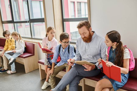 Ein Mann, der Lehrer, sitzt vor einer Gruppe von Kindern in einem hellen und lebhaften Klassenzimmer und liest lebhaft ein Buch, um ihre Fantasie zu beflügeln..