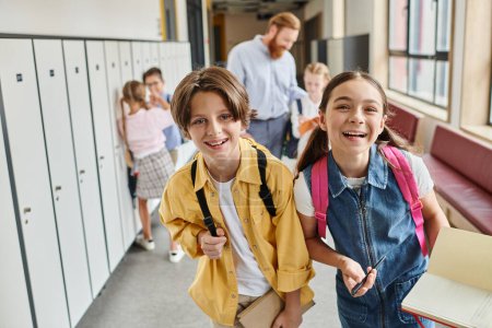 Un grupo diverso de niños camina por un pasillo de la escuela lleno de casilleros coloridos, charlando y riendo mientras se dirigen a su próxima clase.