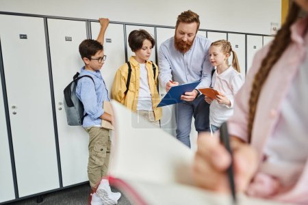 Téléchargez les photos : A man teacher is instructing a group of kids standing near lockers in a brightly lit classroom. - en image libre de droit