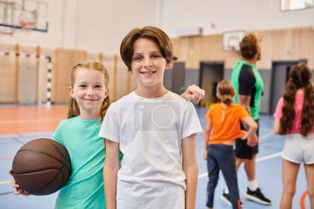 Foto de Dos niños, un niño y una niña, de pie uno al lado del otro, sosteniendo una pelota de baloncesto y sonriendo felizmente. - Imagen libre de derechos