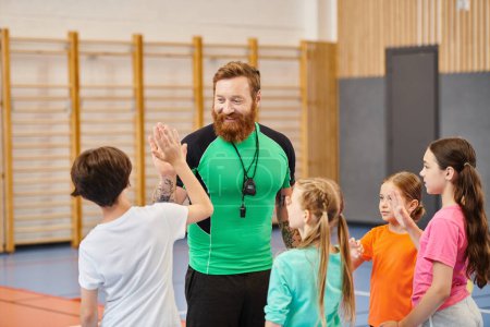 A bearded man stands confidently in front of a group of children, engaging them in a lively classroom setting.