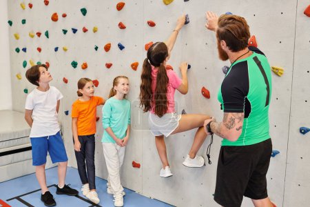 Photo for A diverse group of young children stand side by side on a colorful climbing wall, while their teacher guides them through the challenge. - Royalty Free Image