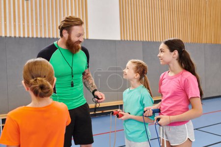 A bearded man, acting as a teacher, energetically communicates with a group of children in a lively, brightly lit classroom.