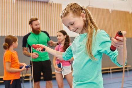 A diverse group of kids engages in an energetic gym session, with a girl confidently holding a jump rope as the male teacher instructs and guides them.