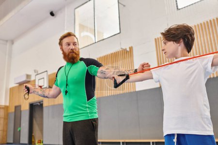 Un instructor barbudo dando consejos a un niño enfocado que practica en un gimnasio soleado.
