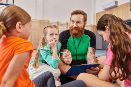 Photo for A bearded man sits on the basketball court surrounded by a diverse group of kids, mentoring and coaching them in an energetic and positive atmosphere. - Royalty Free Image