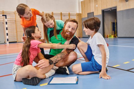 A man teacher sits on the floor surrounded by a diverse group of kids, engaging them in a lively lesson in a bright classroom setting.