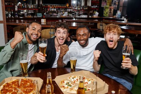 groupe d'amis excités interracial acclamant avec des verres de bière dans le bar, les hommes sur enterrement de vie de garçon