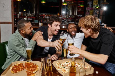 group of excited multicultural friends clinking with glasses of beer in bar, men on bachelor party