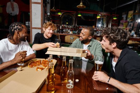 four happy multiethnic friends sharing pizza and drinking beer in bar, men on bachelor party