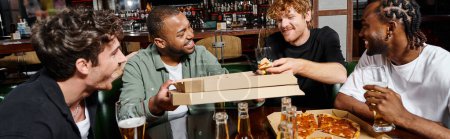 Foto de Cuatro amigos multiétnicos felices compartiendo pizza y bebiendo cerveza en el bar, hombres en despedida de soltero, pancarta - Imagen libre de derechos