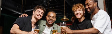 happy interracial men toasting with glasses of beer in bar during bachelor party, friendship banner