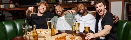 banner of cheerful interracial friends hugging and sitting near pizza and beer, spending time in bar
