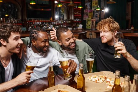 Gruppe fröhlicher multiethnischer Freunde plaudert, hält Biergläser in der Hand und verbringt Zeit in der Bar