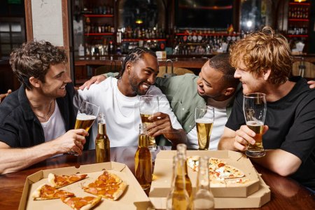 group of happy multicultural male friends chatting and holding glasses of beer, spending time in bar