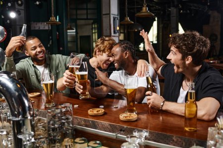 grupo de cuatro amigos masculinos multiétnicos felices sosteniendo vasos de cerveza durante la despedida de soltero en el pub