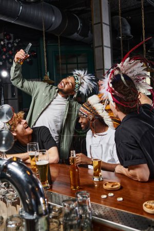 Gruppe junger exotischer Männer in Kopfbedeckung mit Federn, die Bier trinken und Spaß in der Bar haben