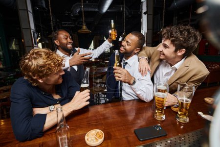 group of interracial happy colleagues in formal wear drinking beer in bar, having fun after work