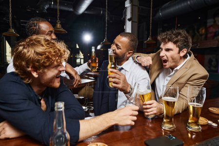 Emotionale und interrassische Kollegen in offizieller Kleidung trinken Bier in der Bar und haben Spaß nach der Arbeit