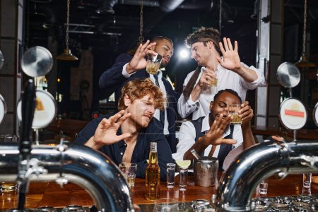 Foto de Cuatro amigos borrachos multiculturales cubriendo rostros de luz brillante, tequila, cerveza y whisky - Imagen libre de derechos