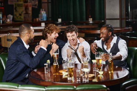 four happy and drunk interracial colleagues having fun after work in bar, alcohol drinks on table