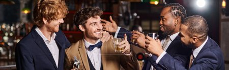 amigos felices en ropa formal felicitando al novio en el bar, hombres interracial sosteniendo una pancarta de whisky