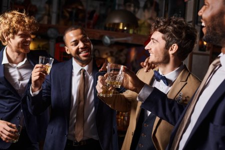 Junggesellenabschied, glückliche interrassische Männer, die mit Gläsern Whiskey in der Bar anstoßen, Bräutigam und Trauzeugen