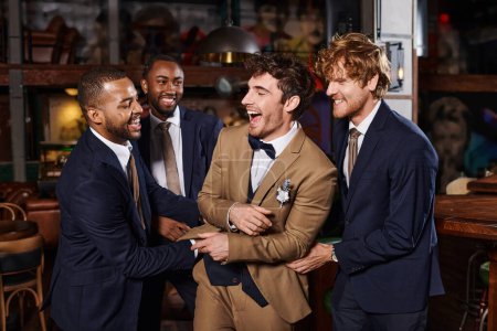 bachelor party, excited interracial men congratulating friend in bar, best men and groom in suits