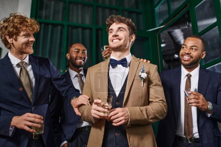 Junggesellenabschied, fröhliche gemischtrassige Männer gratulieren Freund in Bar, Trauzeugen und Bräutigam in Anzügen