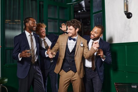 Junggesellenabschied, multiethnische Trauzeugen und Bräutigam lachen, während sie mit Gläsern Whiskey stehen