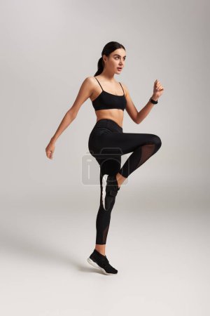Foto de Mujer bastante deportiva en ropa deportiva negro con rastreador de fitness en la muñeca calentamiento sobre fondo gris - Imagen libre de derechos