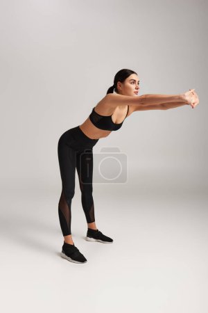 Foto de Mujer atlética en ropa deportiva negra con rastreador de fitness en la muñeca que se extiende hacia atrás en el fondo gris - Imagen libre de derechos