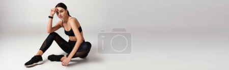 Foto de Joven deportista en uso activo con rastreador de fitness en la muñeca sentado sobre fondo gris, pancarta - Imagen libre de derechos