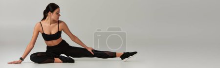 flexible woman in active wear and sneakers stretching legs on grey background, motivation banner