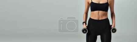 Foto de Vista recortada de la deportista en desgaste activo negro haciendo ejercicio con mancuernas sobre fondo gris, pancarta - Imagen libre de derechos
