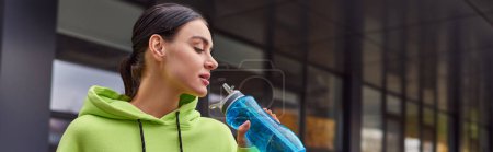pretty sportswoman in lime color hoodie drinking water from bottle after workout, horizontal banner