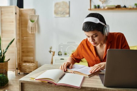 Konzentrierte kurzhaarige Frau mit Kopfhörern, die von zu Hause aus das Lehrbuch, die Bildung betrachtet
