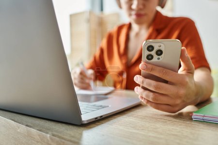 Photo for Cropped focused view of laptop and mobile phone in front of young student in orange shirt, education - Royalty Free Image