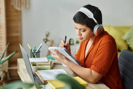 Photo for Young female student studying hard and taking notes while on remote lesson, education at home - Royalty Free Image