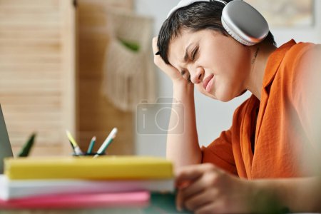 confused young brunette woman with tattoo on neck and headphones studying hard at home, education