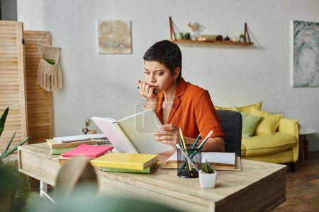 jeune étudiante réfléchie assise au bureau et étudiant son matériel avec stylo à la main, éducation
