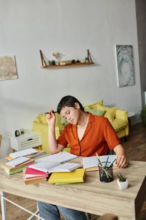 Foto de Plano vertical del estudiante cansado trabajador que se sienta en el escritorio con la pluma en el libro de texto de la lectura de la mano - Imagen libre de derechos