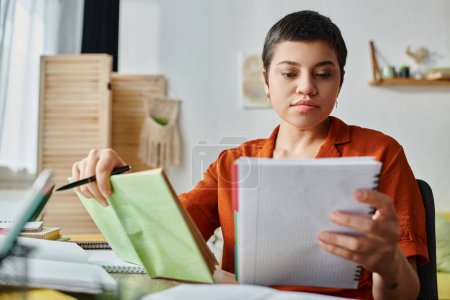 Téléchargez les photos : Femme aux cheveux courts concentré étudiant dur sur ses notes et tenant un stylo, éducation à la maison - en image libre de droit