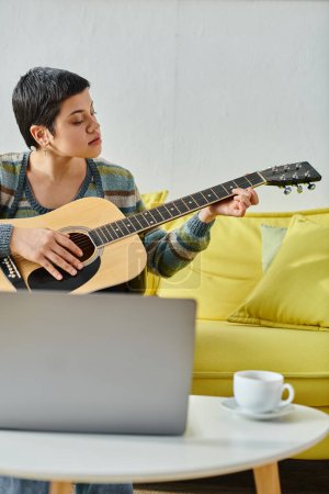 Foto de Disparo vertical de la joven mujer de pelo corto sentado delante de la computadora portátil aprender a tocar la guitarra - Imagen libre de derechos